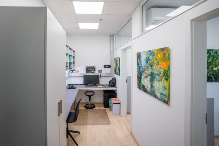 Durchgang im Büro von Schinnerl IT mit Gemälden an den Wänden und Arbeitsplätzen mit PCs und Bildschirmen im Gang